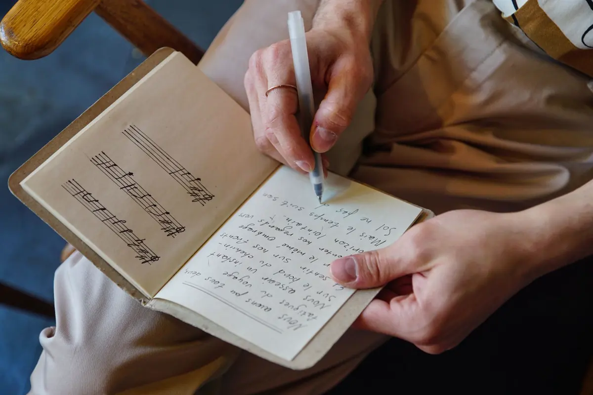 Mãos escrevendo letra de música num caderno